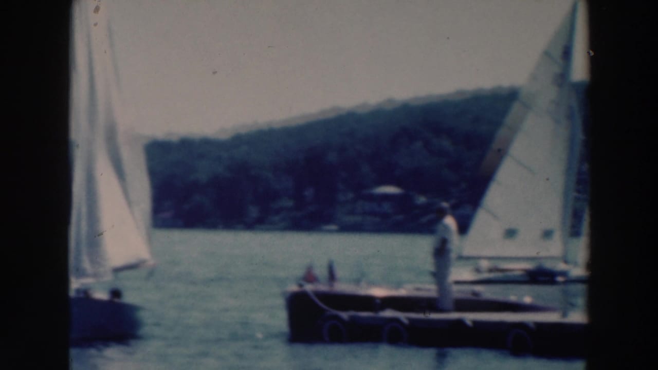 A 1964 lake sailing scene near Tustin, Wisconsin, with racing sailboats passing a small dock or pontoon and distant shoreline.