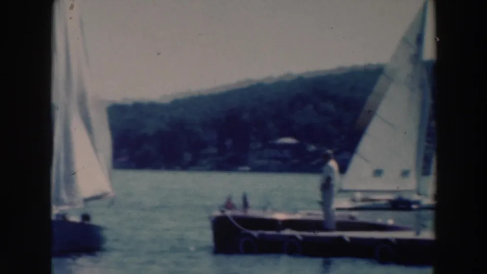 A 1964 lake sailing scene near Tustin, Wisconsin, with racing sailboats passing a small dock or pontoon and distant shoreline.