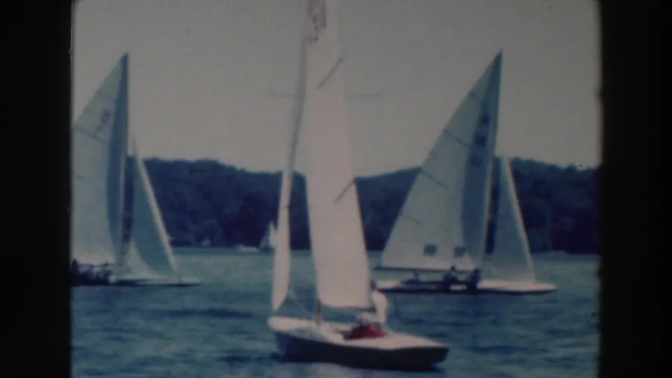 1964 home-movie view of several sailboats clustered on a Wisconsin lake, including a foreground boat with a red shirt or item.