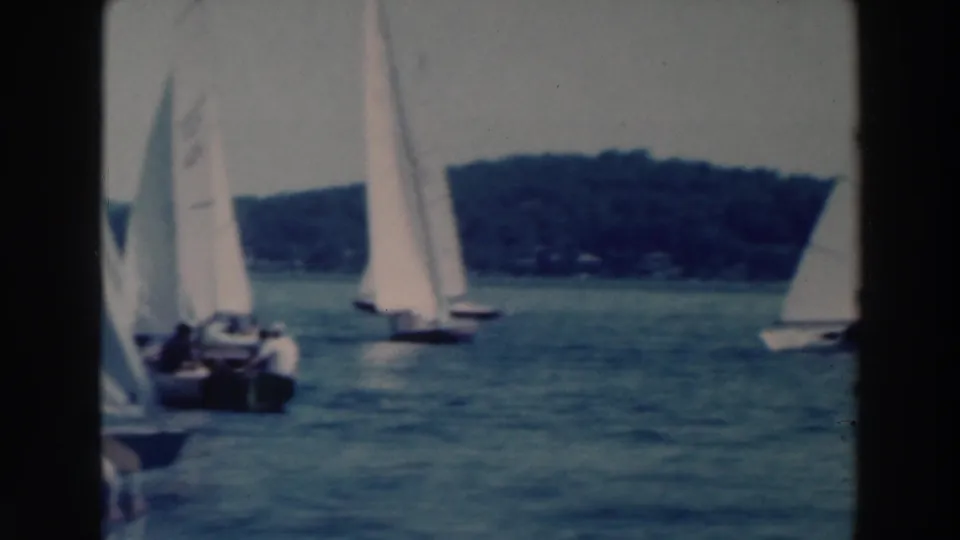 1964 Tustin, Wisconsin home-movie frame showing a closer sailboat at left and other sailboats spread across the lake.
