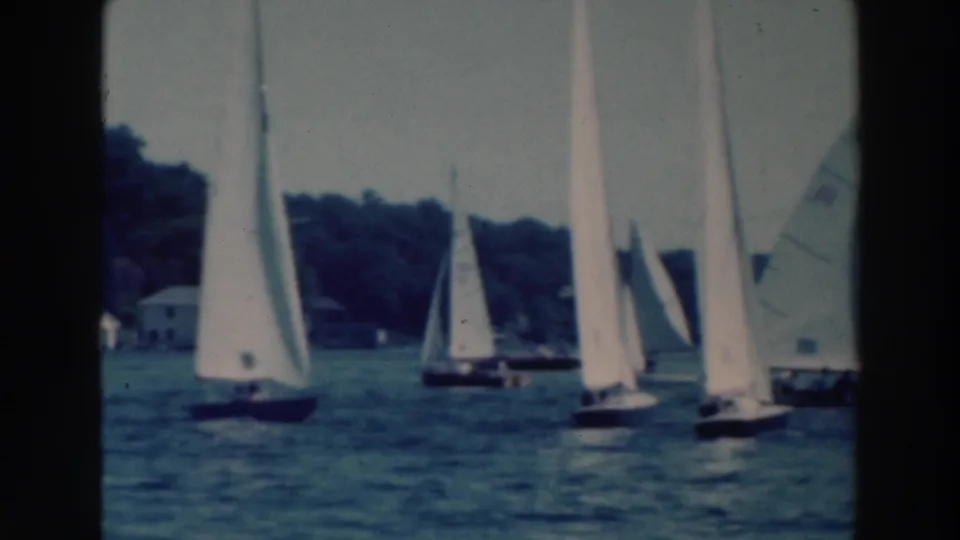 1964 Tustin, Wisconsin home-movie frame showing a group of sailboats near a wooded lake shore, with soft focus and 8mm borders.