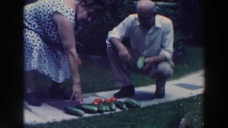 1964 Wisconsin backyard frame showing an elderly couple arranging cucumbers and tomatoes on a walkway.
