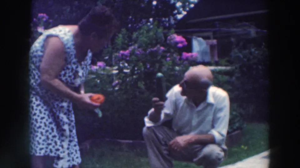 In 1964 Tustin, Wisconsin, a woman holding garden vegetables leans toward a squatting man on the lawn.