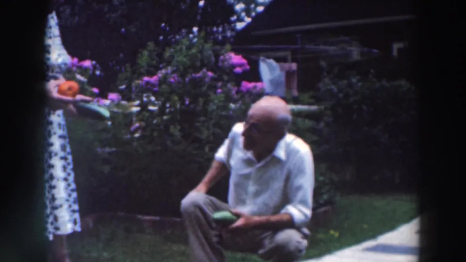 A man in a white shirt crouches in the Tustin, Wisconsin garden as a woman stands beside him holding vegetables.