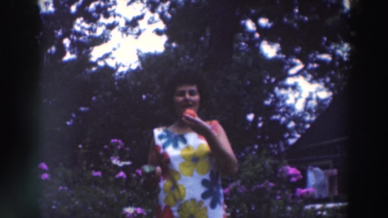 Woman in a white floral dress eating a red apple in a garden.