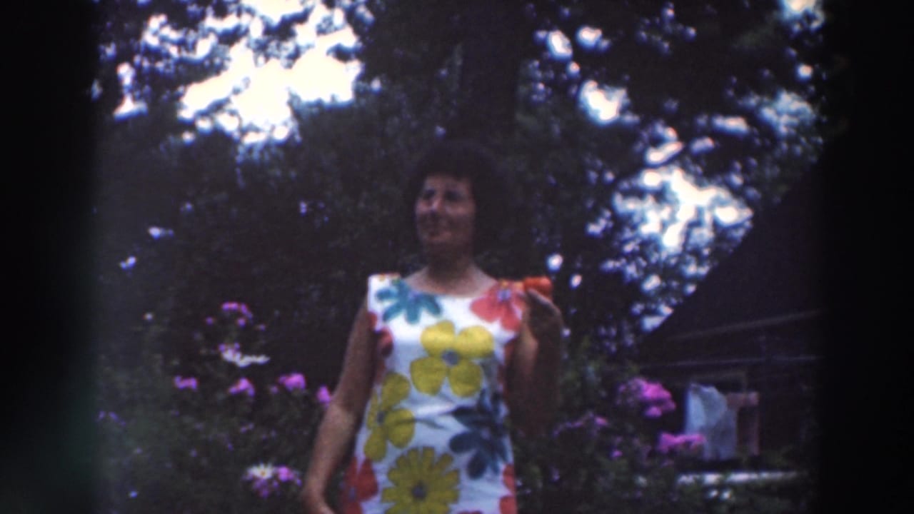 Smiling woman in a floral dress standing outdoors near flowers and trees.
