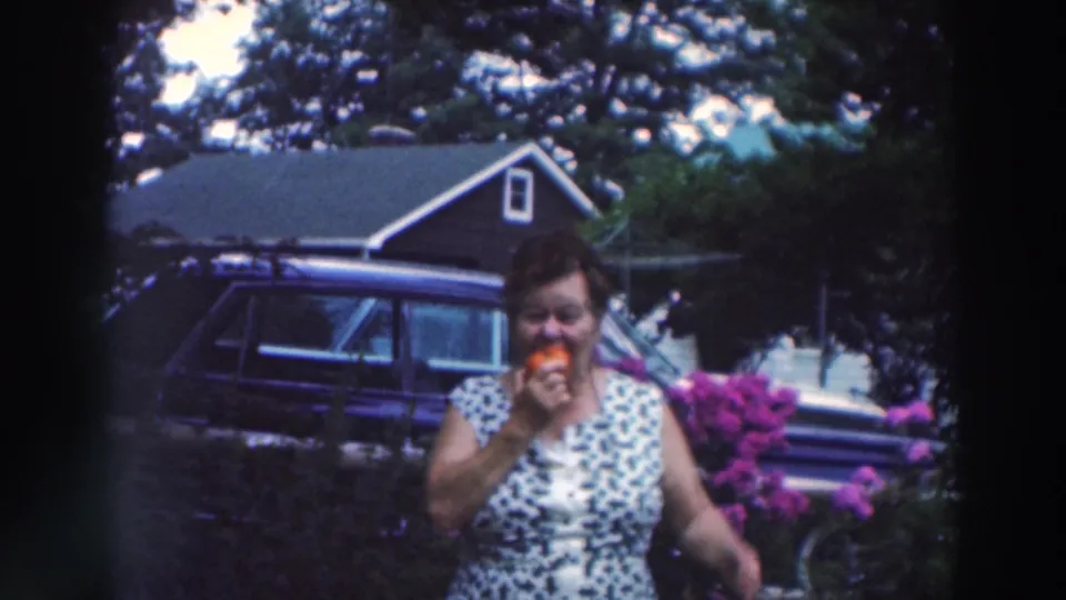 The woman continues eating ice cream, smiling near garden flowers with the station wagon and house visible behind her.