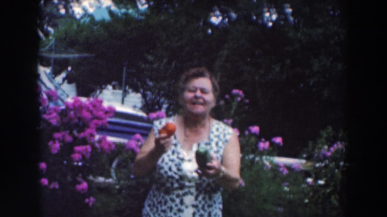 Adult woman in a blue and white dress stands in a garden holding a red tomato and green pepper.
