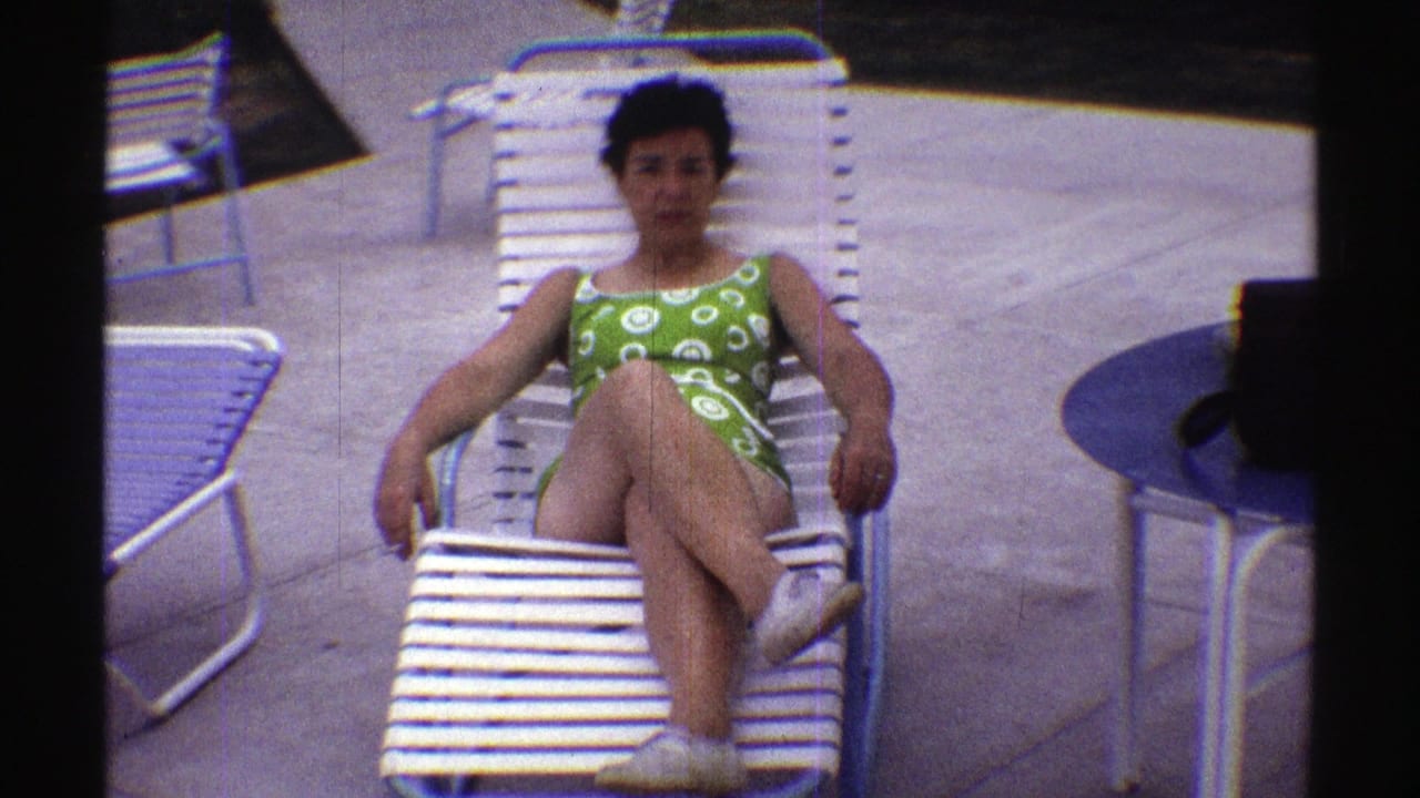 Woman in a green patterned swimsuit reclines on a white lounge chair beside a pool deck.