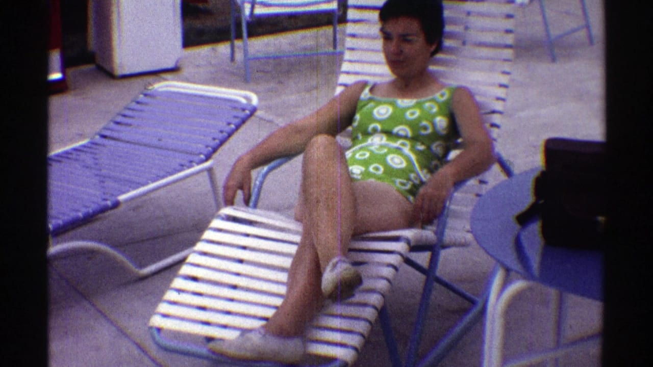 Woman seated with legs crossed on a white lounge chair near a blue table and black bag.