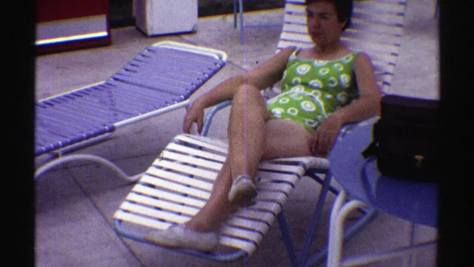 A closer 8mm frame shows the woman reclining in a green swimsuit on the white slatted chair, with another lounge chair beside her.