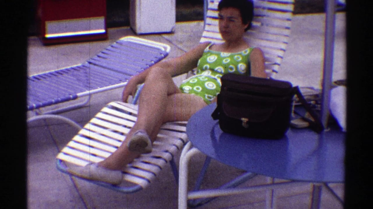 Woman reclines on a striped lounge chair with a black handbag on a blue table in front of her.