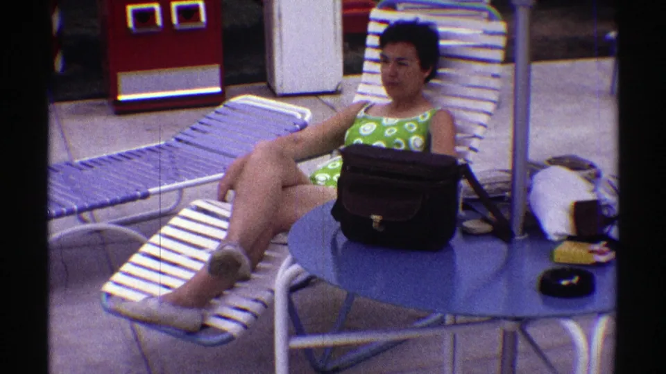 The final frame keeps the woman in a relaxed poolside pose, with the blue table, black handbag, and striped lounge chairs clearly visible.
