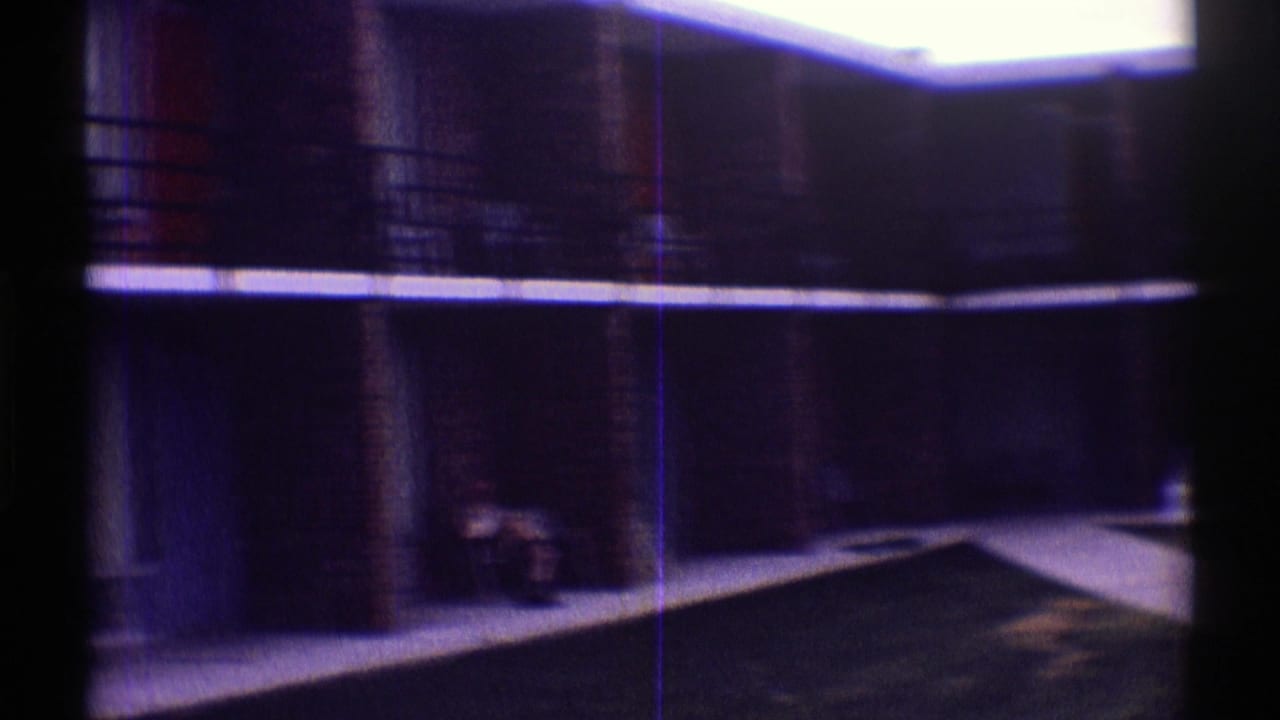 Dark motel balcony and courtyard walkway with a small seated figure.
