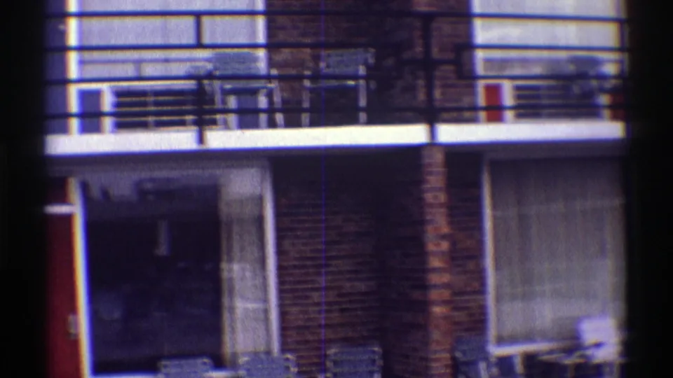 Late-1960s motel exterior in Nebraska showing balcony railings, brick walls, curtained windows, doors, and courtyard chairs.