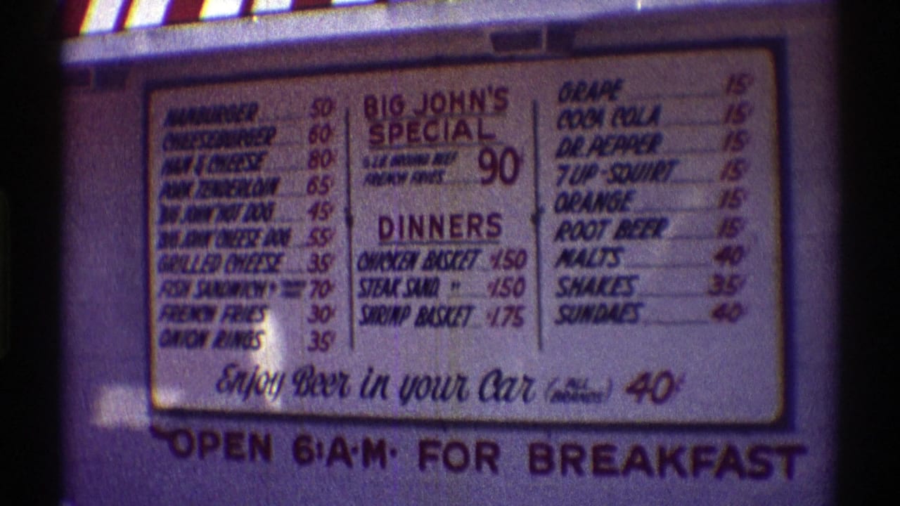 1969 Nebraska 8mm frame of a fast food menu board listing burgers, dinners, beverages, and Big John's Special.