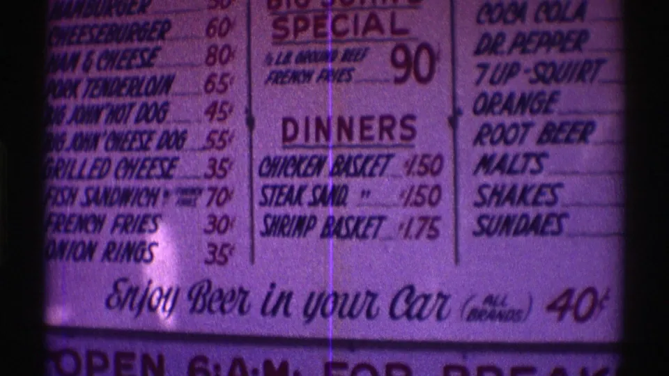Purple-tinted 1969 Nebraska 8mm frame showing a restaurant menu with burgers, dinner baskets, drink options, and a beer-in-car price line.