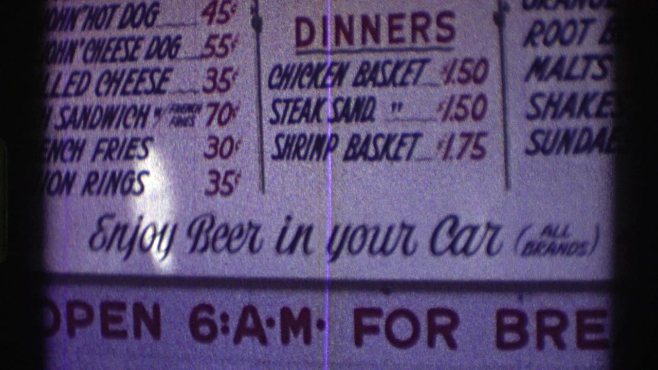 1969 Nebraska 8mm frame showing a backlit roadside menu with dinner listings, cents pricing, and "Enjoy Beer in your Car" text.