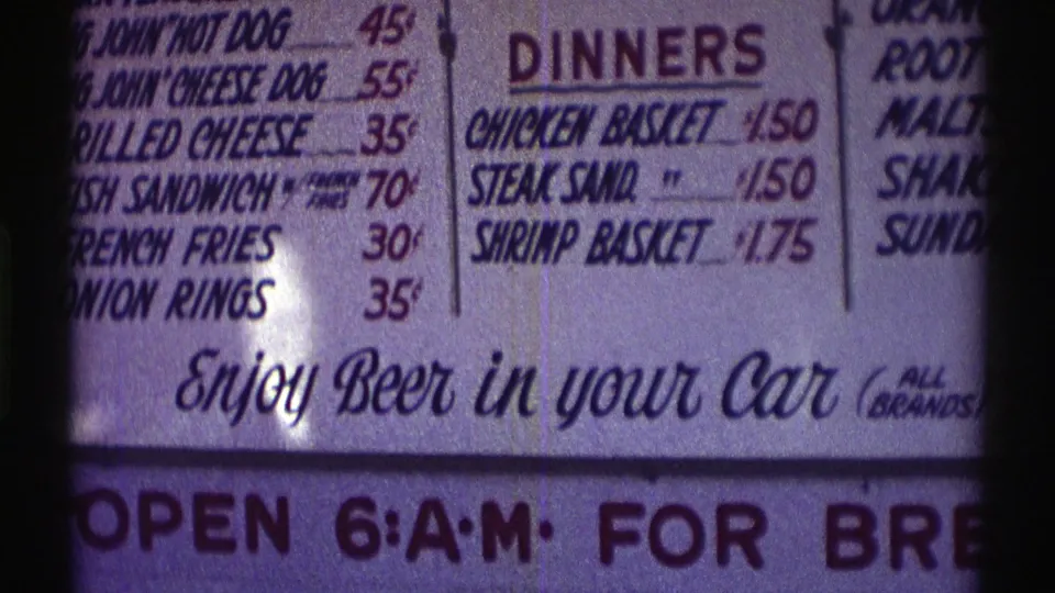 1969 Nebraska close-up of a roadside menu board showing hot dogs, grilled cheese, dinners, and the beer-in-car slogan.