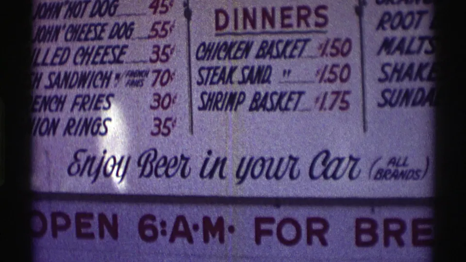 1969 Nebraska 8mm view of a drive-through menu with onion rings, basket dinners, and a prominent beer-in-car message.