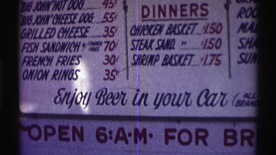 1969 Nebraska frame of the drive-through menu board, centered on dinner listings and the "Enjoy Beer in your Car" phrase.
