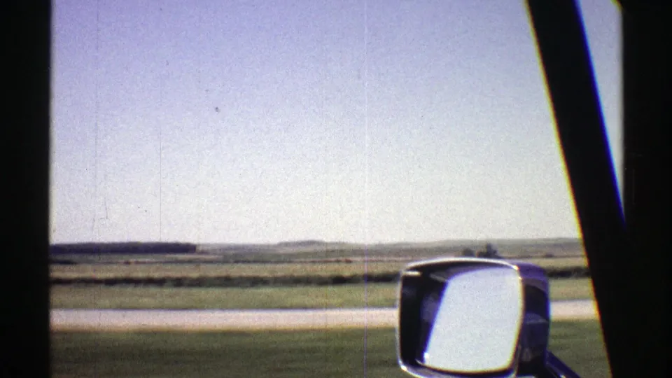 Nebraska 1969 8mm frame showing a passenger-side view over a roadside and broad plains with the car mirror visible.