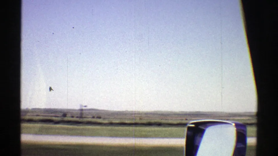 1969 Nebraska 8mm travel frame showing flat roadside fields and distant low terrain through the car window.
