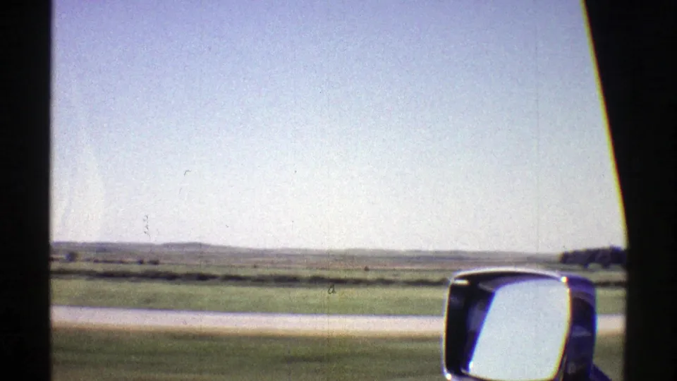 1969 Nebraska passenger-window view with a side mirror, broad rural landscape, and pale blue sky.