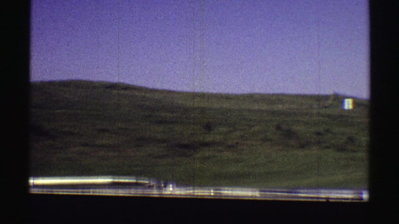 Green hillside seen through a car window, with a small white object near the distant ridge.