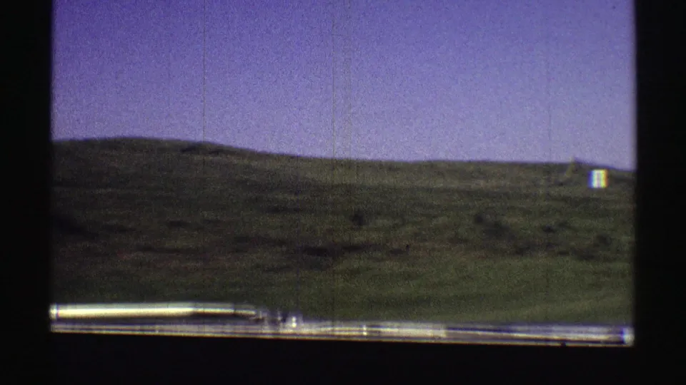 1969 Nebraska roadside view through a car window, showing a green hill, blue sky, and a small white distant object on the slope.