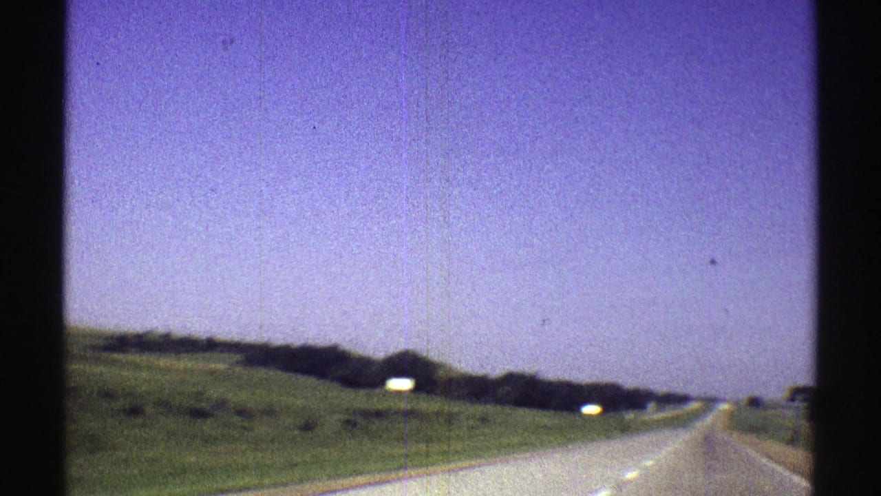 1969 Nebraska 8mm frame showing a rural highway ahead, green embankments, distant signs, and visible film borders.