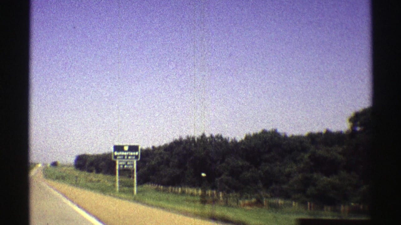 Rural highway shoulder with a distant blue Sutherland exit sign beside trees and open sky.