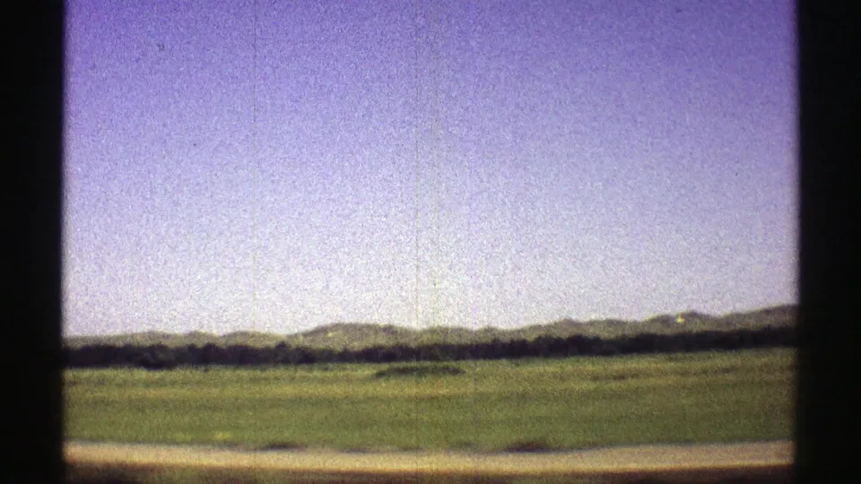 1969 Nebraska 8mm frame looking across open fields toward distant low hills under a pale blue sky.