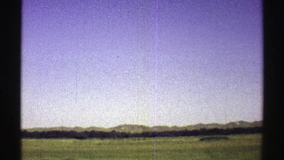 1969 Nebraska 8mm frame showing open green prairie, a distant tree line, and low hills beneath a pale purple sky.