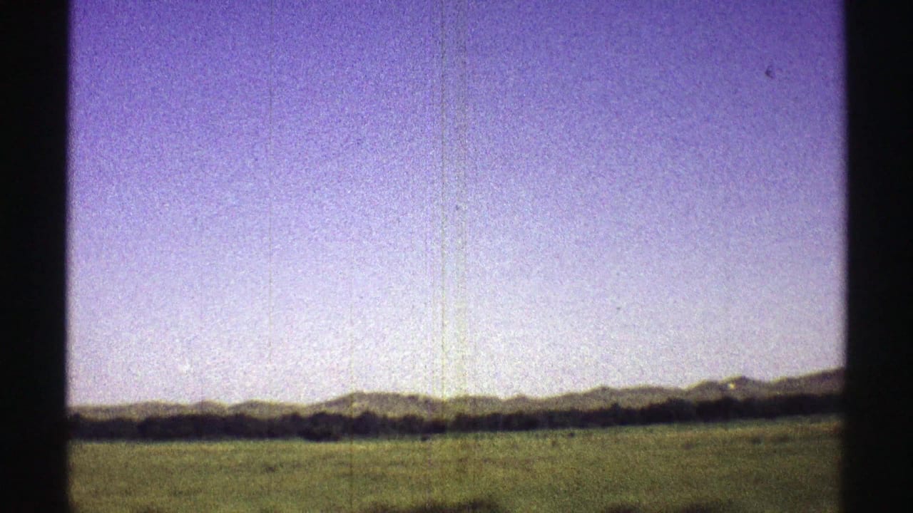 1969 Nebraska 8mm frame with a broad field, far hills, and a dark vertical car-window obstruction at center.