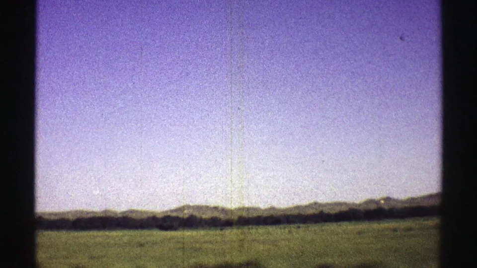 1969 Nebraska 8mm frame with a broad field, far hills, and a dark vertical car-window obstruction at center.