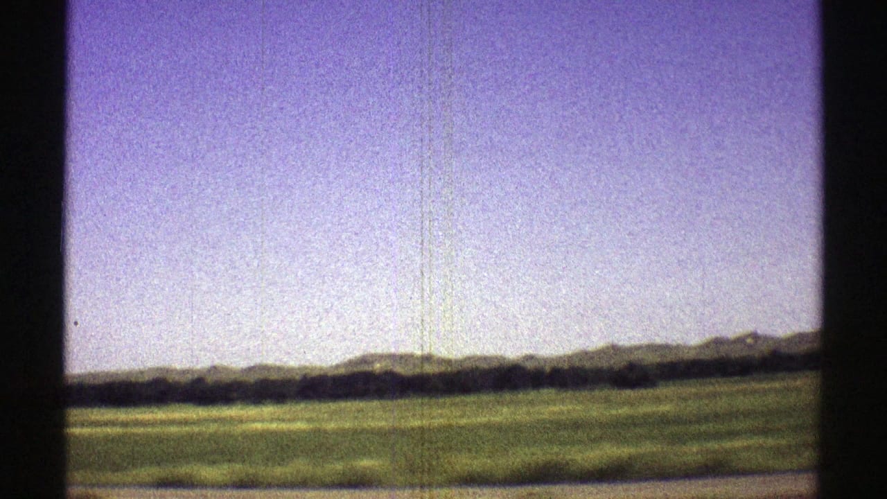 1969 8mm Nebraska landscape showing open grassland, distant low hills, and a dark tree line at the edge of the frame.
