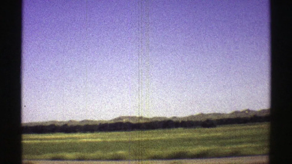 1969 8mm Nebraska landscape showing open grassland, distant low hills, and a dark tree line at the edge of the frame.