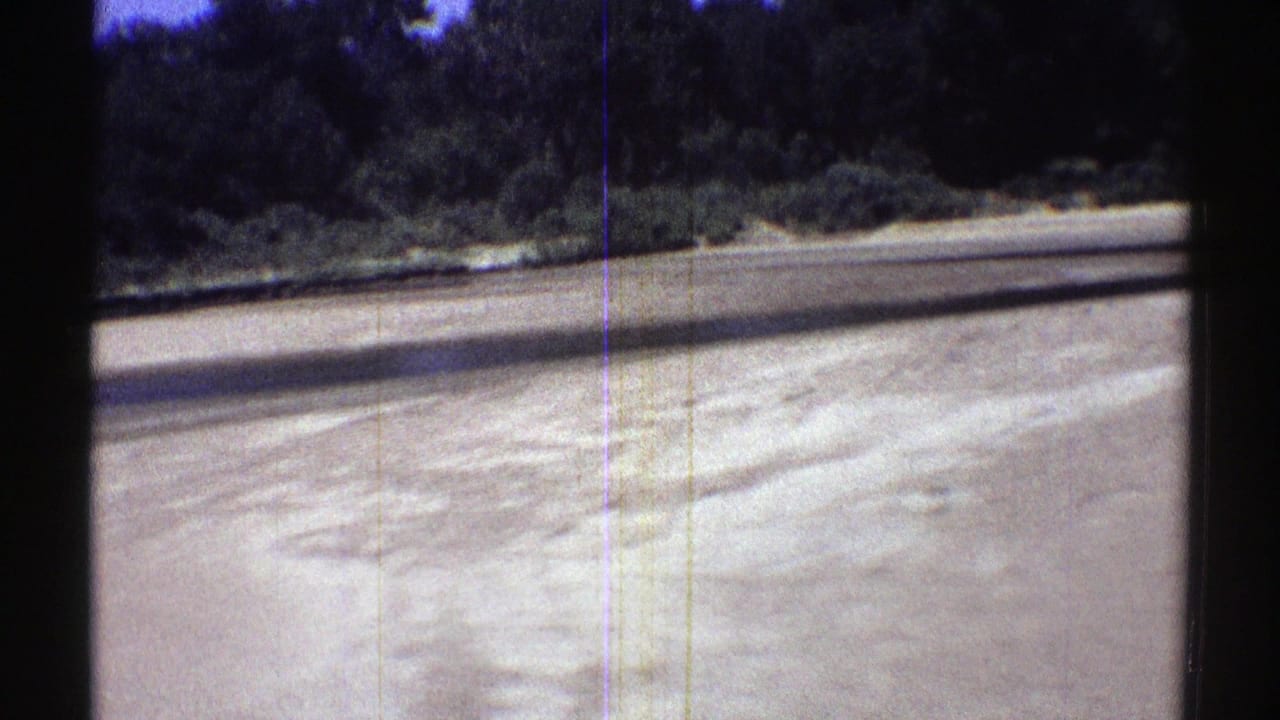 Nebraska stream bank with a broad pale sand bar, shallow water, and thickets of trees in 1969 home-movie footage.