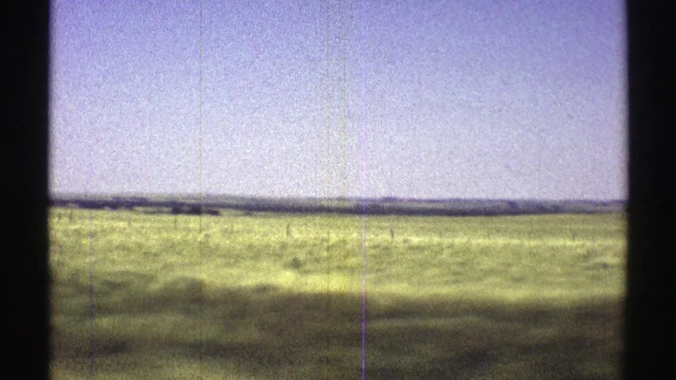 1969 Nebraska 8mm frame showing open grassland, pale sky, a low horizon, and soft film grain from a moving countryside view.
