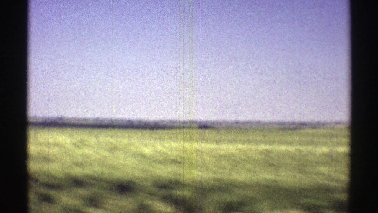 1969 Nebraska 8mm frame showing a green field beneath a pale sky, with dark gate edges and visible film grain.