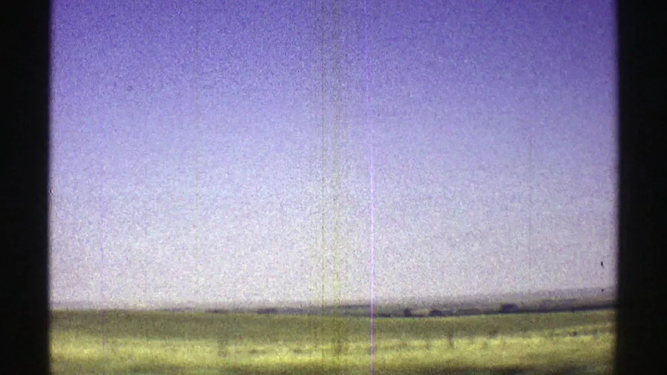 1969 Nebraska 8mm view of an open green field and distant horizon, marked by grain and vertical film scratches.