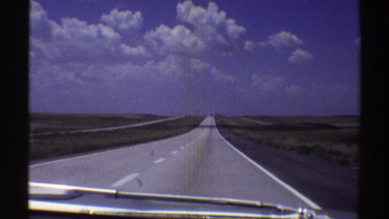 Open highway stretching toward the horizon with clouds overhead and a windshield wiper below.