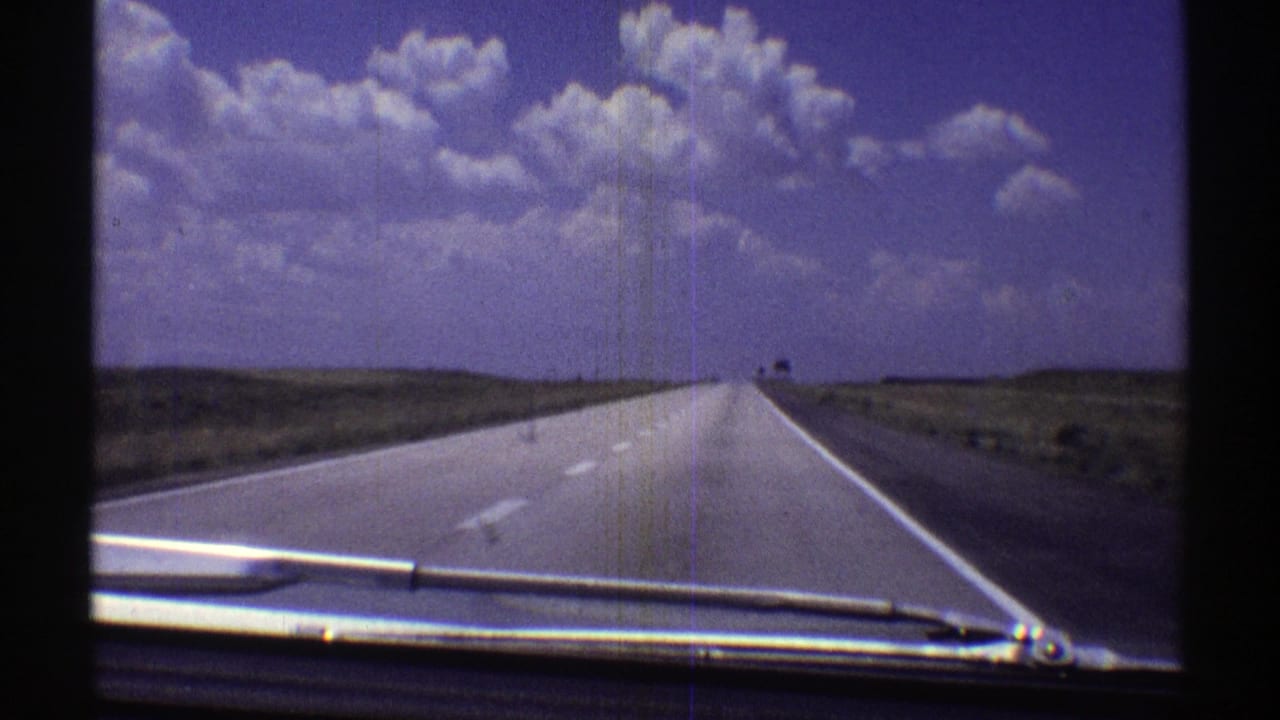 1969 Nebraska 8mm frame showing a car-dashboard view down a long, open highway with plains and large clouds ahead.