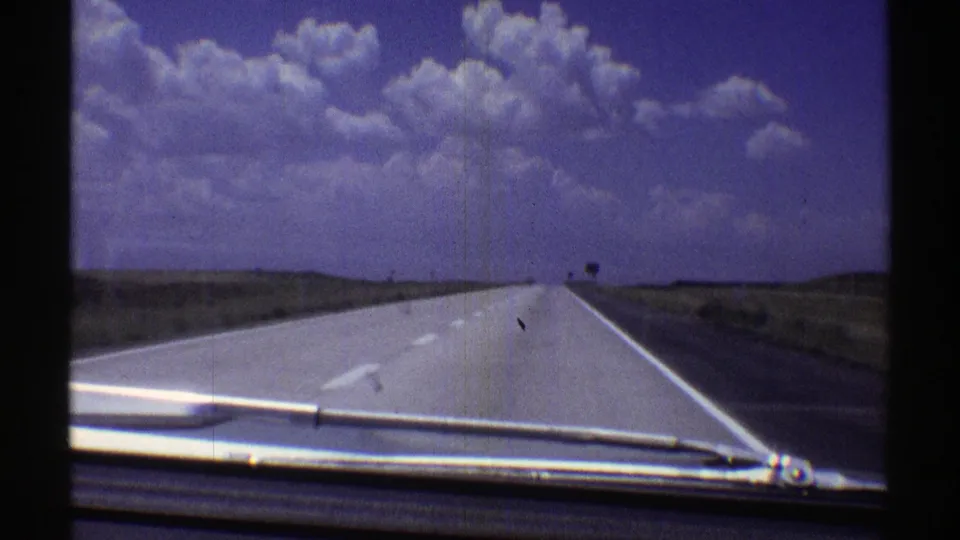 1969 Nebraska 8mm travel frame showing a forward car view along a rural highway bordered by open land and a distant horizon.