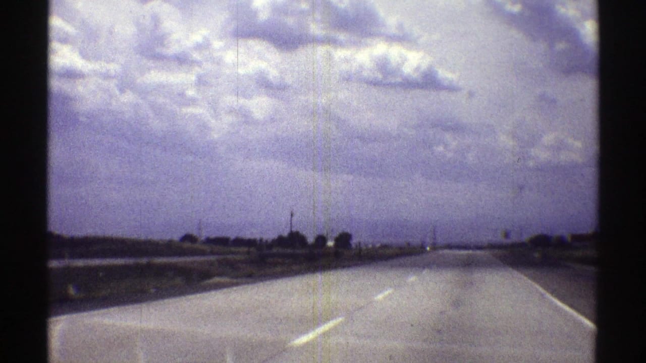 Roadway curves gently ahead across flat land beneath broken clouds.