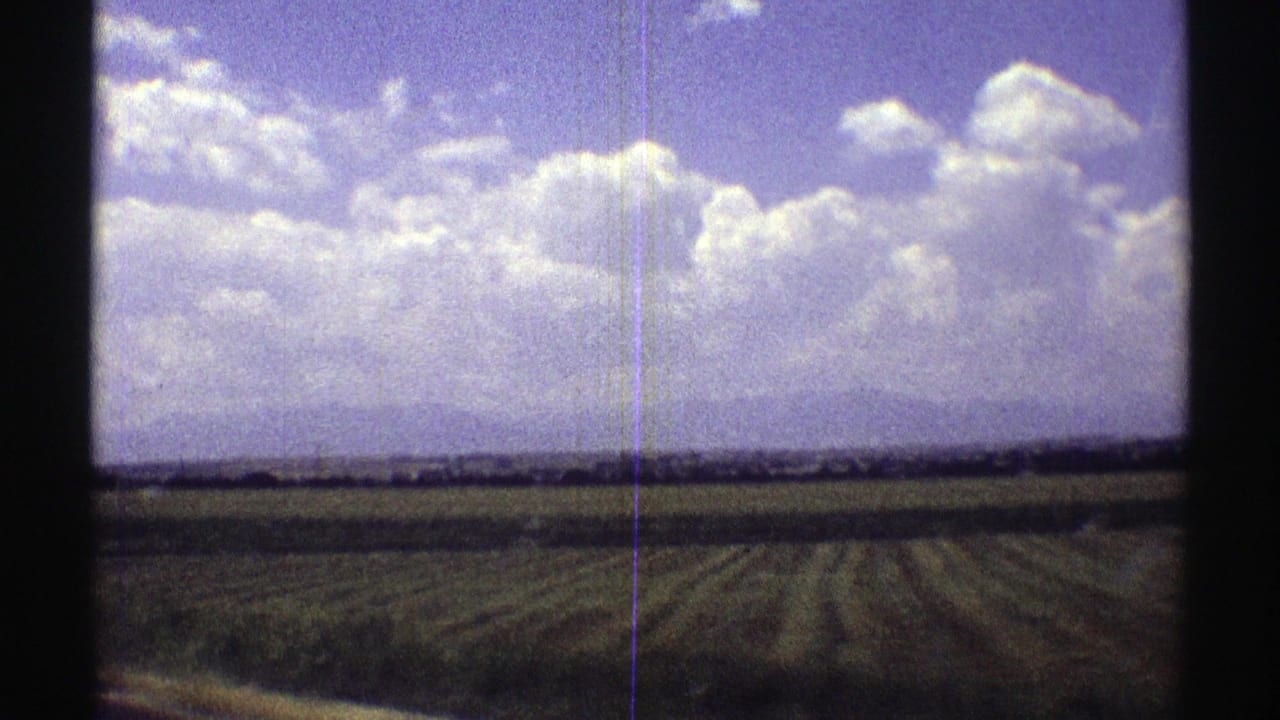 Rural Nebraska farmland appears beyond dark contact-sheet borders, with cultivated rows and a broad 1969 8mm sky view.
