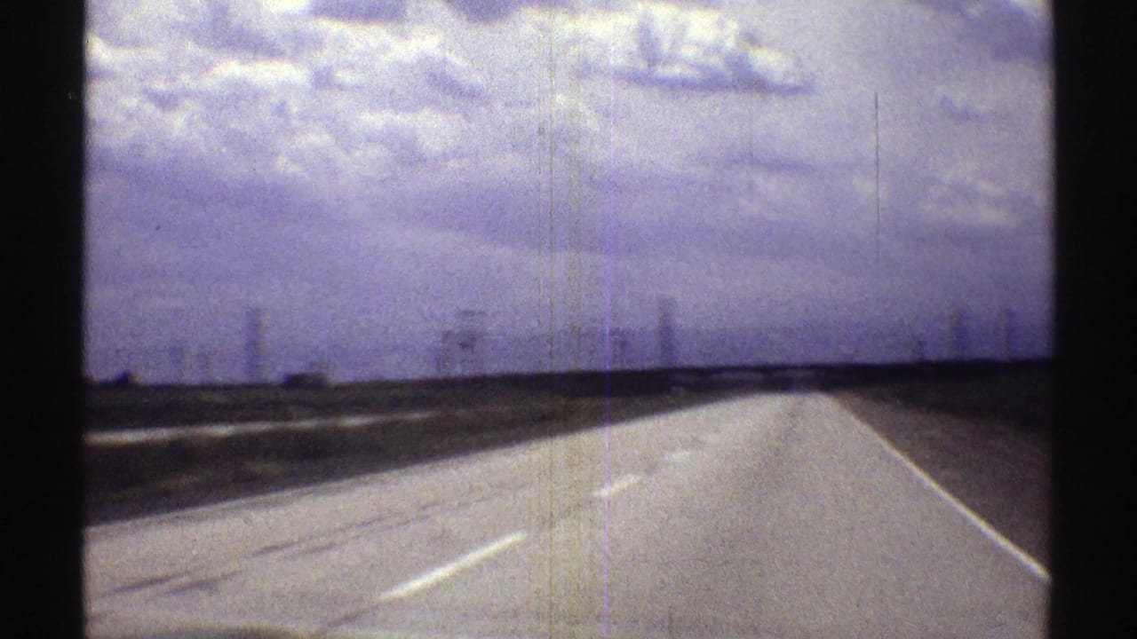 Rural highway stretching toward a cloudy horizon from a moving vehicle perspective.