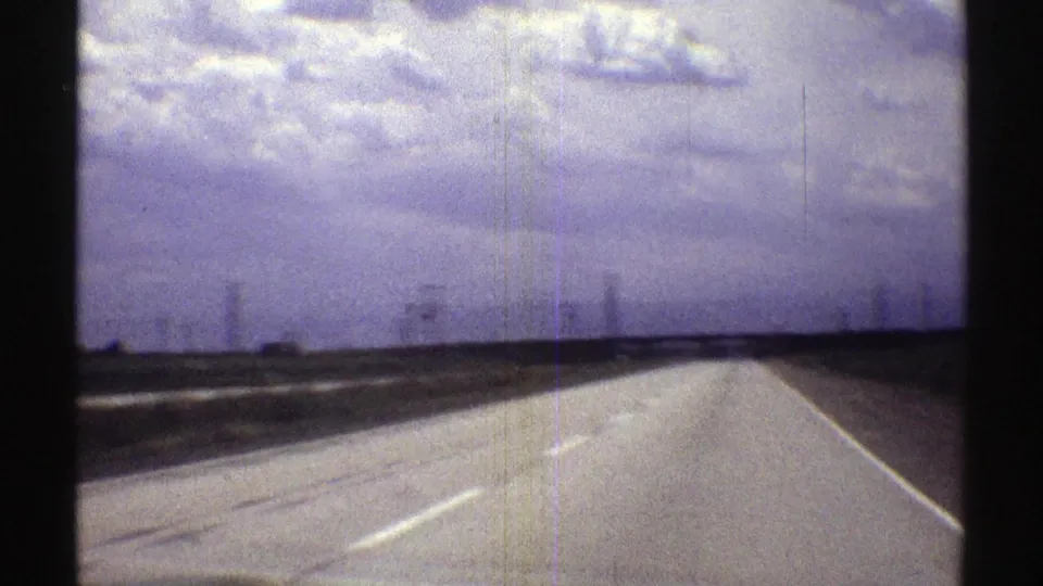 1969 Nebraska 8mm frame showing a rural road under a broad cloudy sky, filmed from a traveler’s viewpoint.