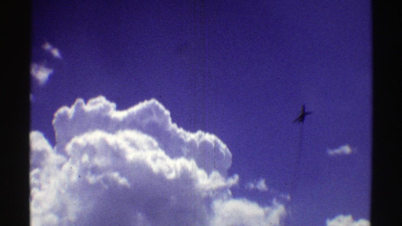 Bright clouds against deep blue sky with a small airplane silhouette at right.
